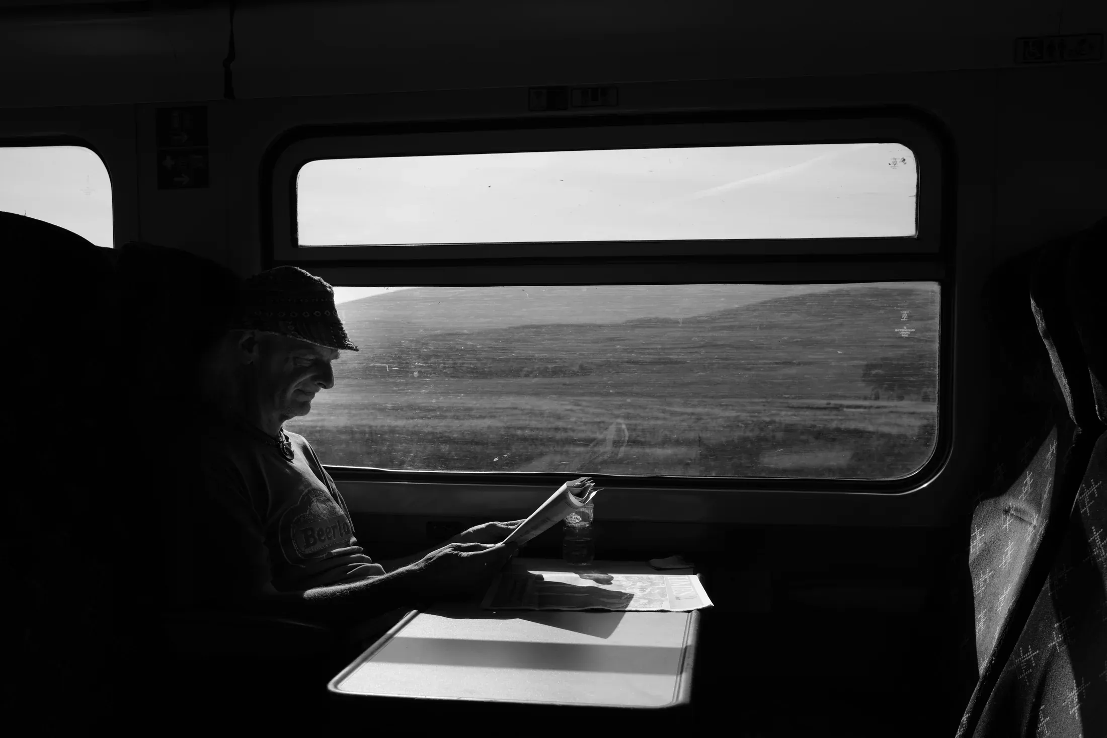 Man seated alone at a train table, looking at his phone in black and white.