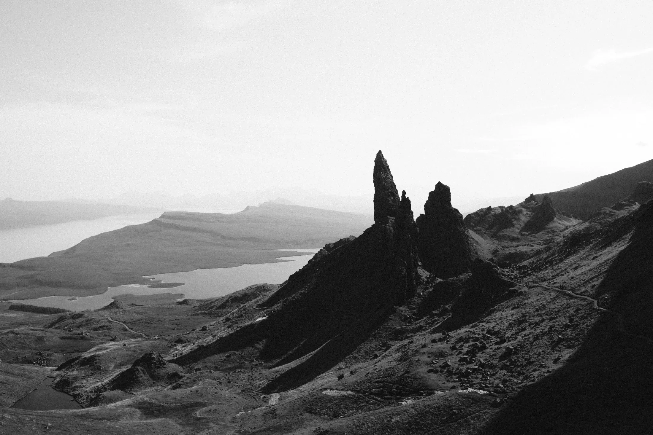 Black and white coastal view from a jagged rock formation toward layered islands.