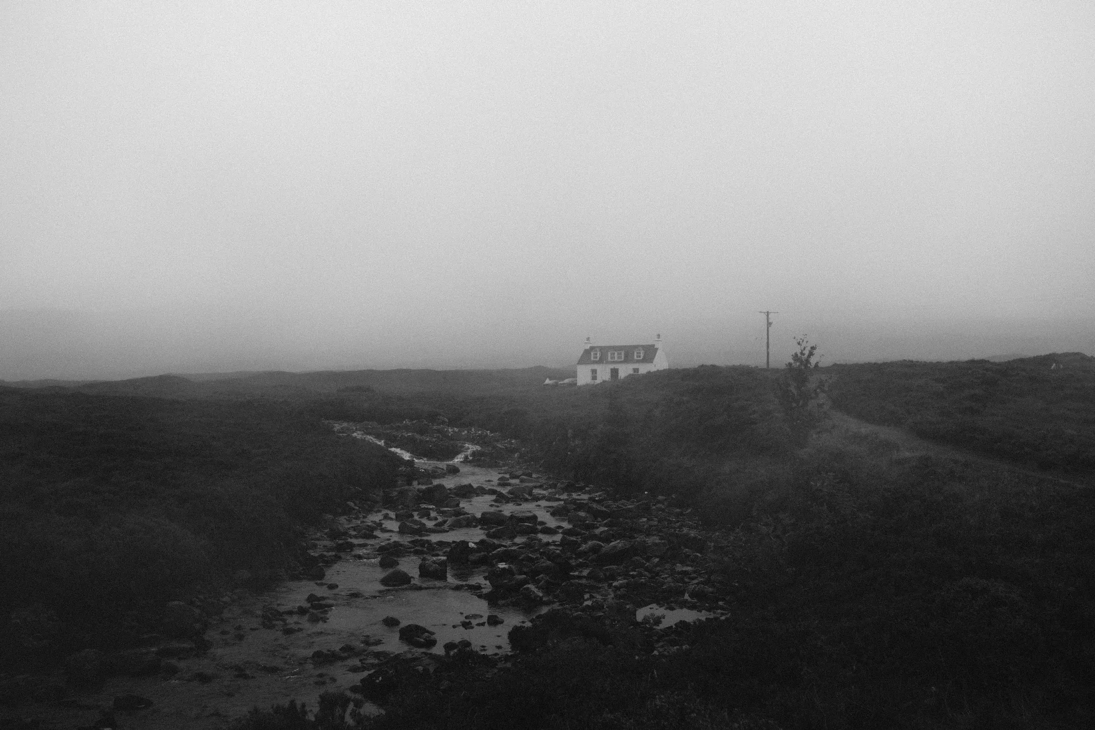 Small white house isolated in a foggy treeless landscape beside a rough track.