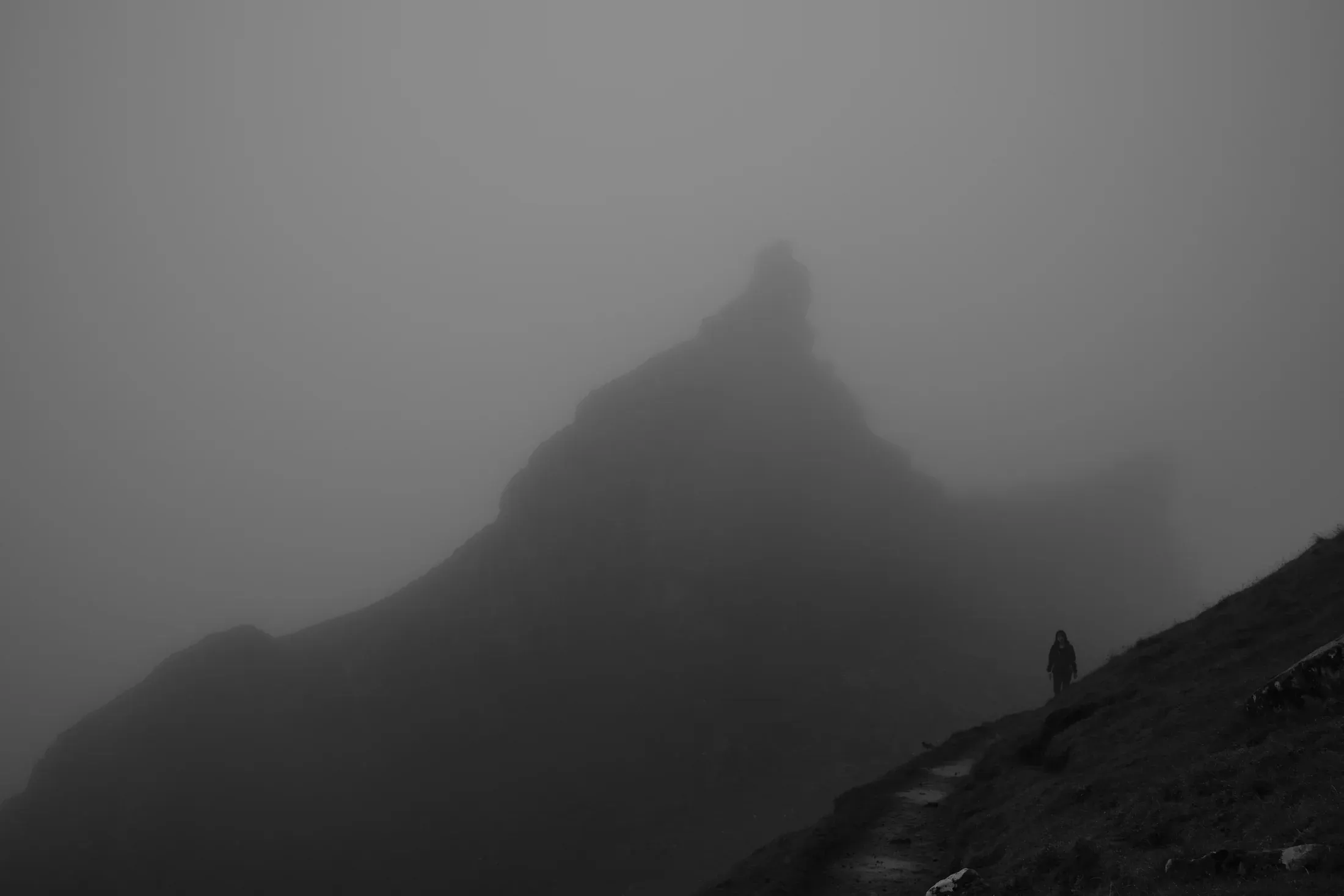 Dark mountain peak emerging through dense fog in black and white.
