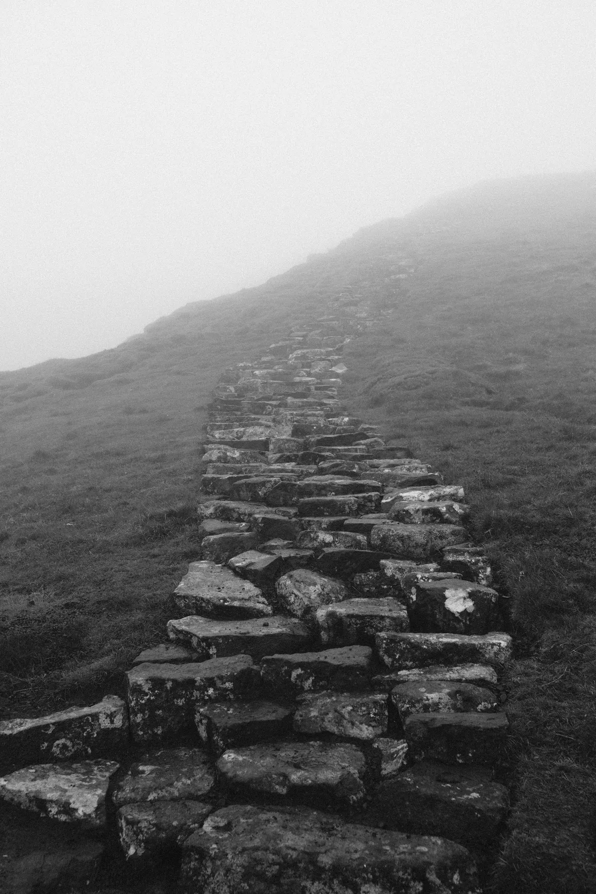 Black and white stone path climbing toward a mountain disappearing into mist.