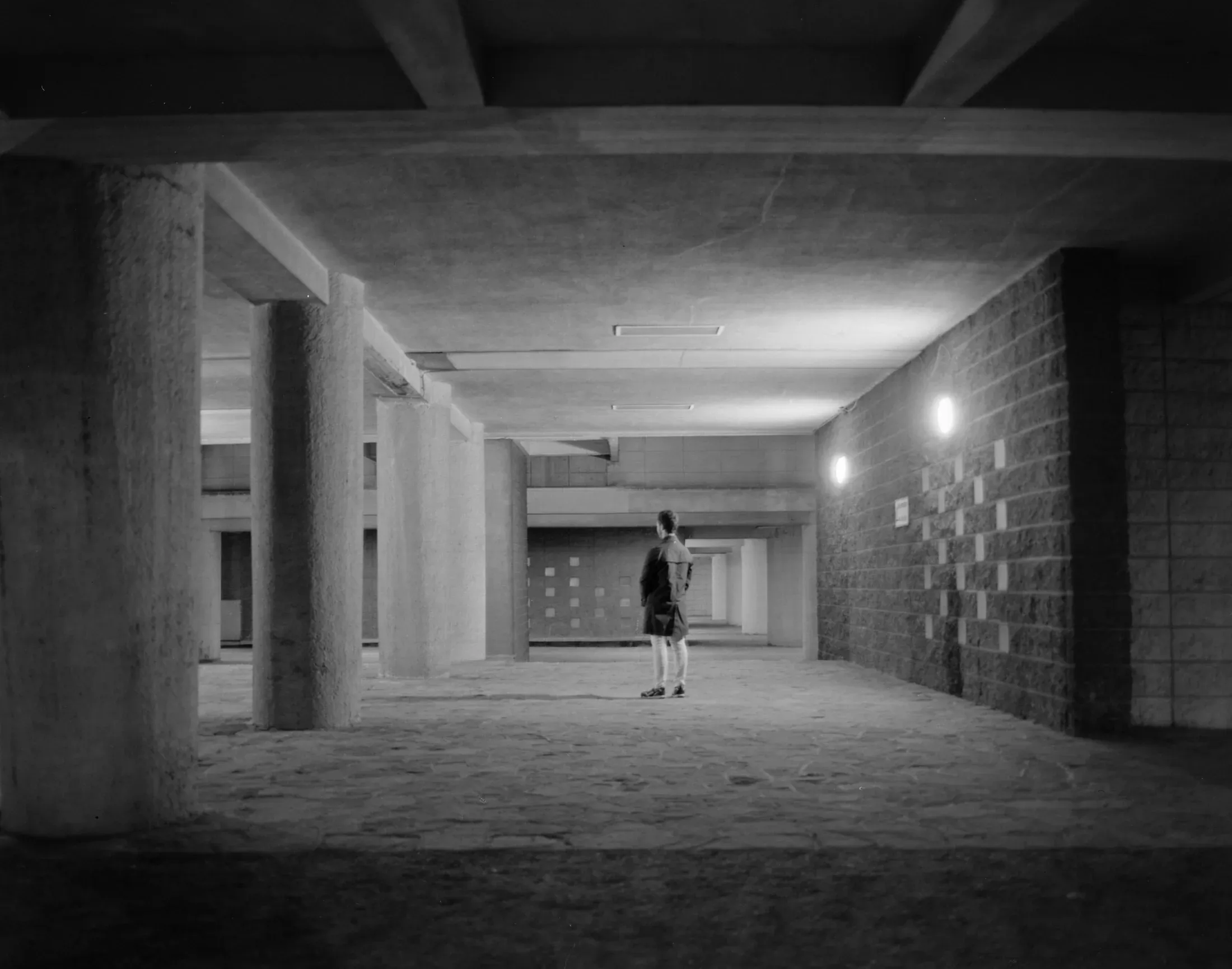 Lone figure standing in a vast unfinished concrete interior lit from one side.