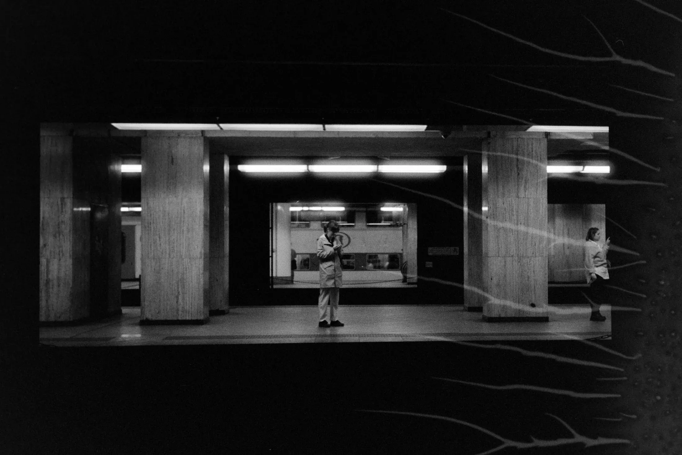 Small child standing alone on a brightly lit metro platform in black and white.
