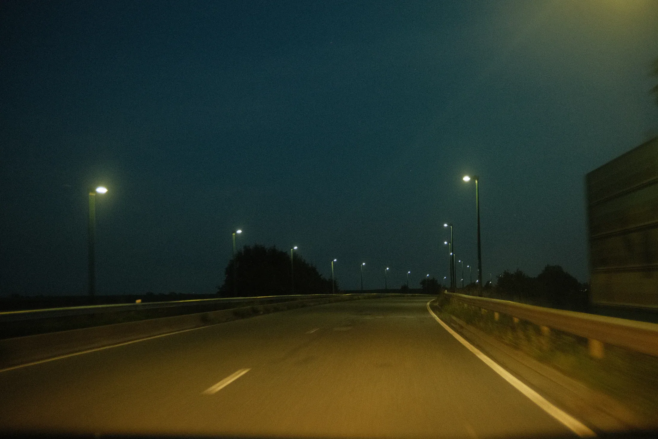 Empty motorway curving beneath green-tinted streetlights on a foggy night.