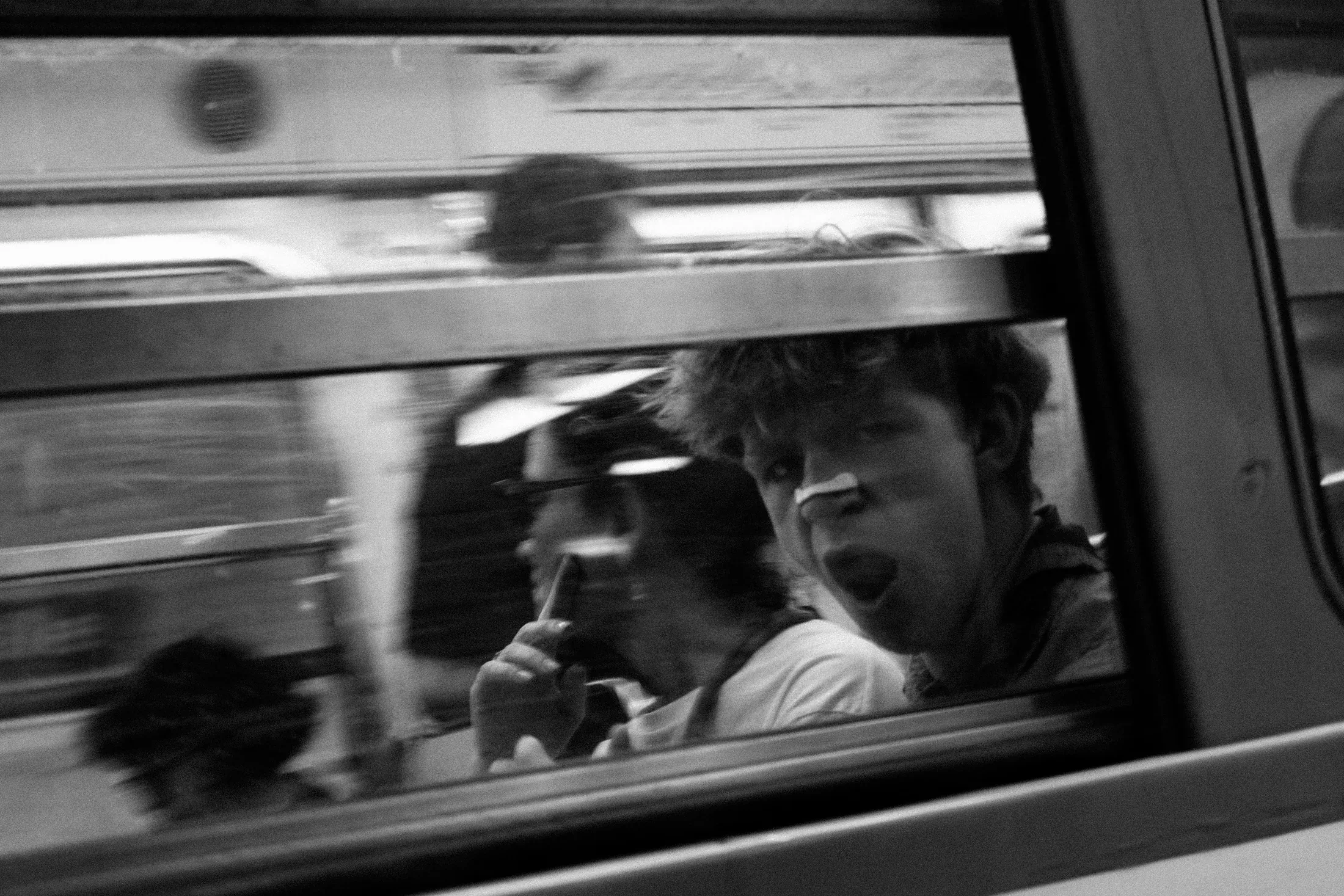 Two train passengers seen through a carriage window as another train passes in a blur.