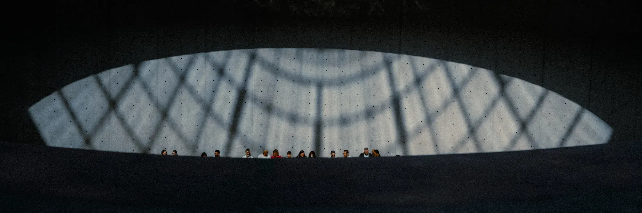 Row of visitors framed beneath a broad geometric opening in a dark interior.