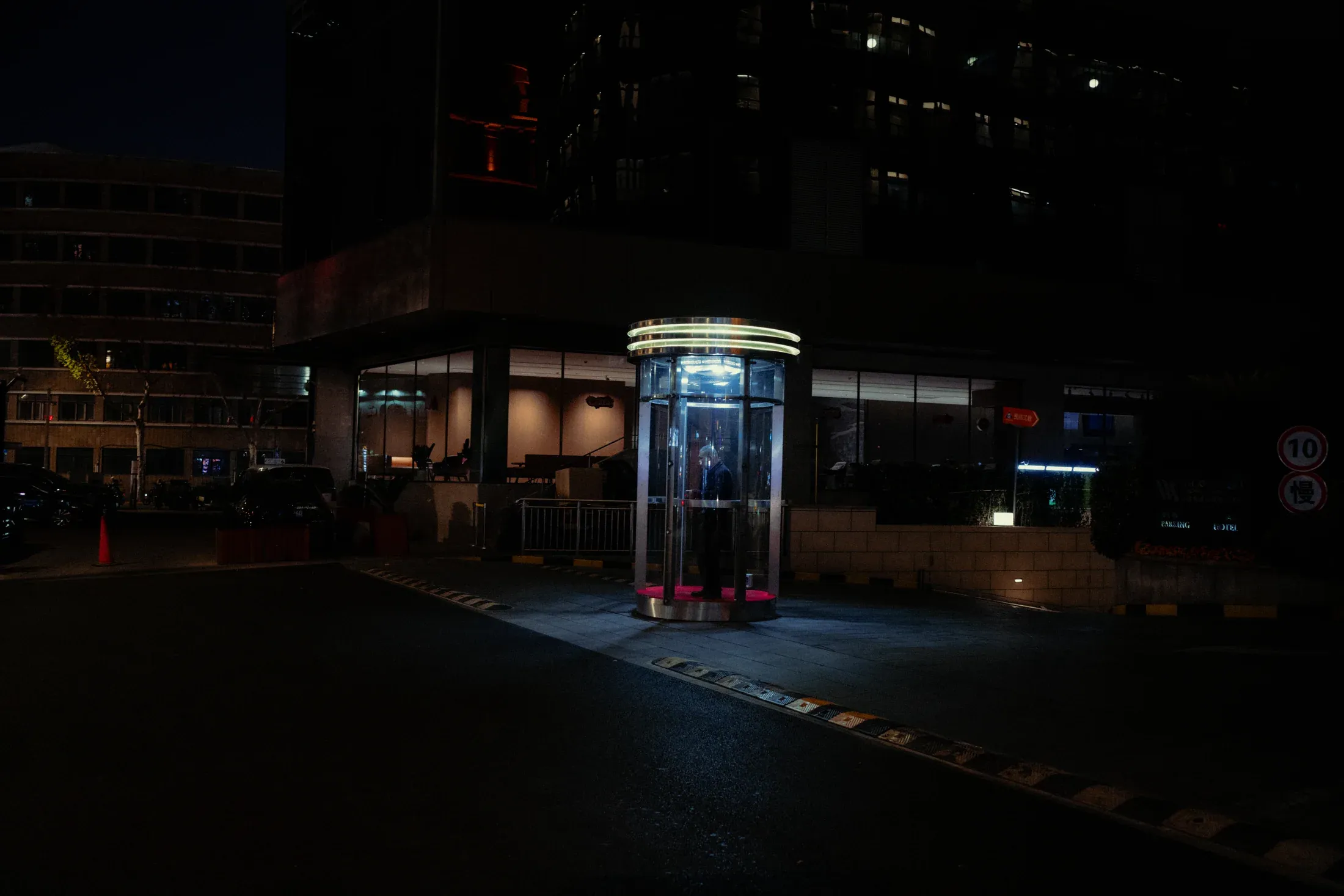 Security guard standing inside a brightly lit glass booth on a dark Shanghai street.