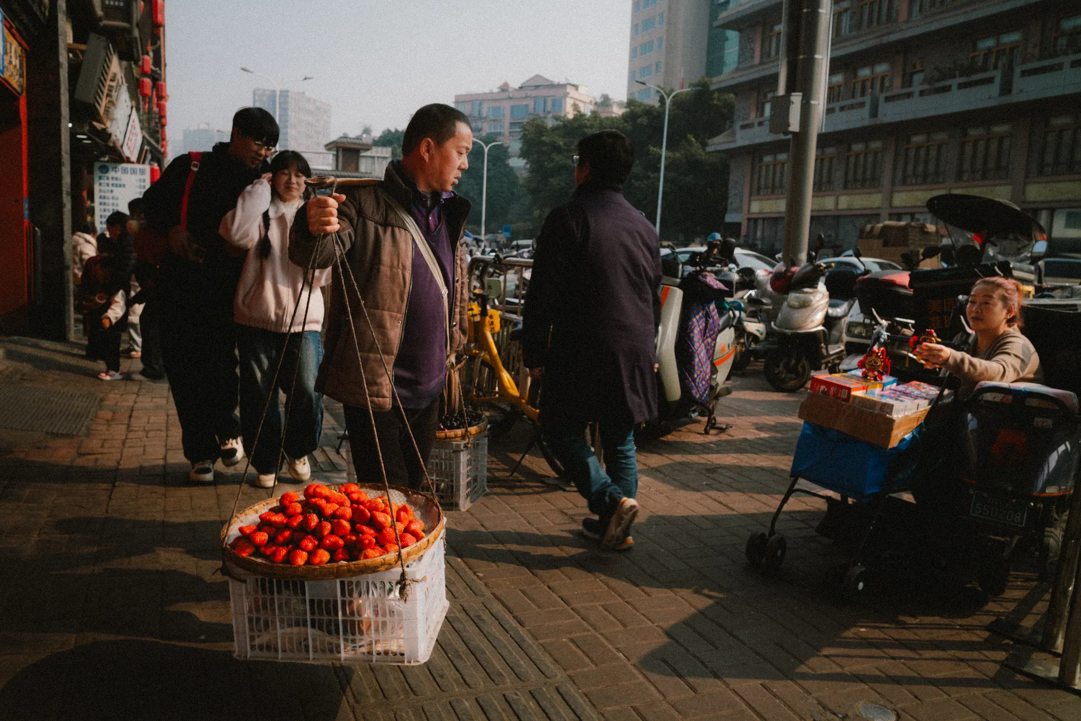 Crowded Chengdu pavement market with baskets of red fruit in late-afternoon light.