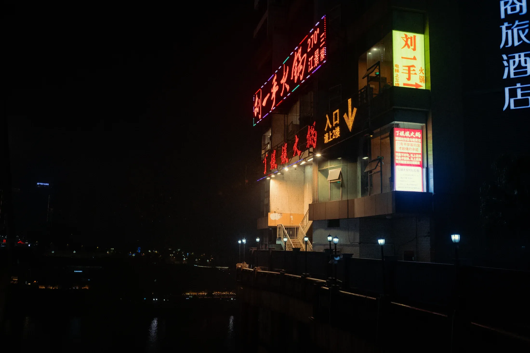 Neon hotel signs glowing against a black night sky in Chongqing.