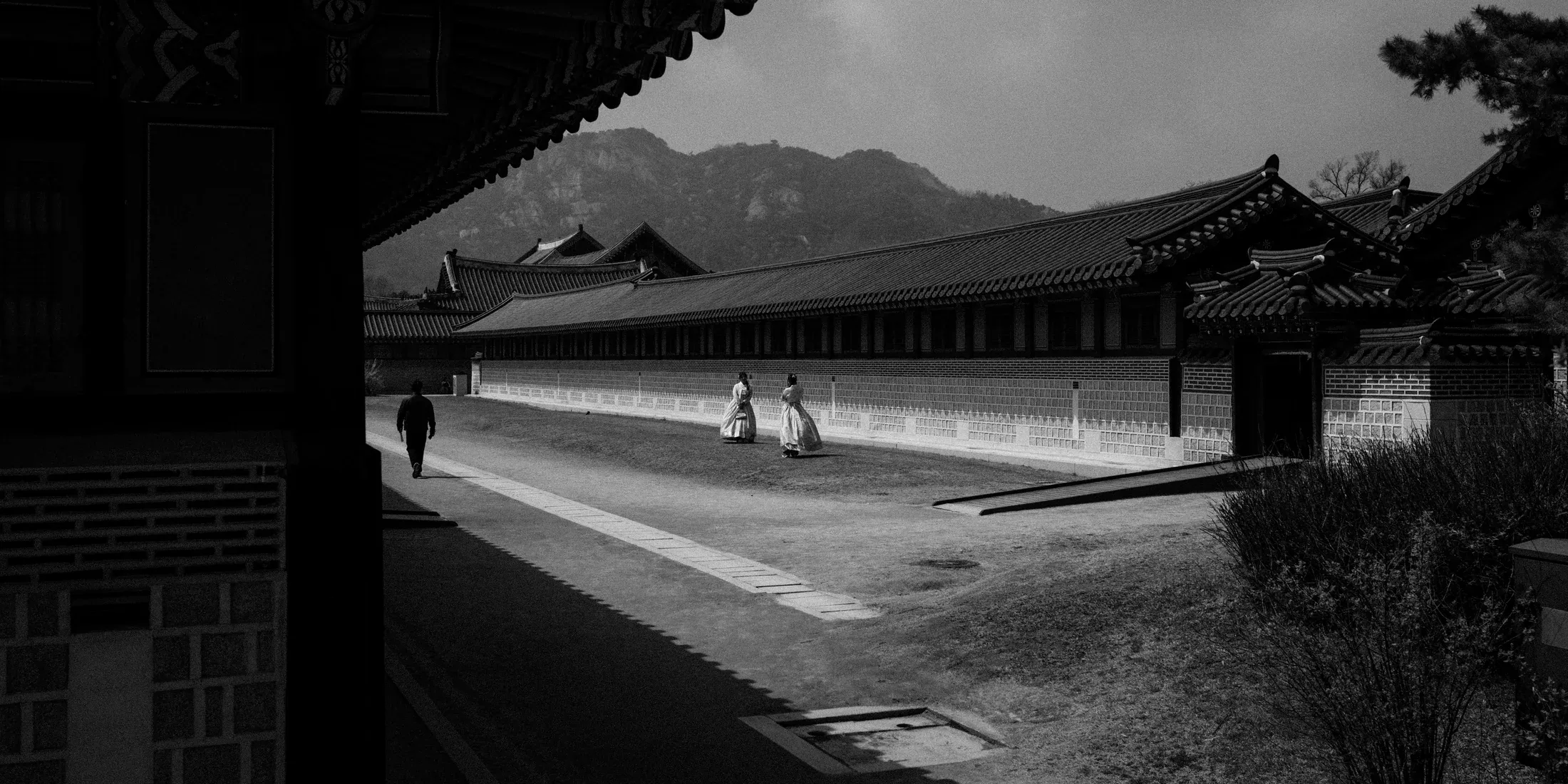 Black and white palace courtyard seen from deep shadow with mountains behind the roofline.