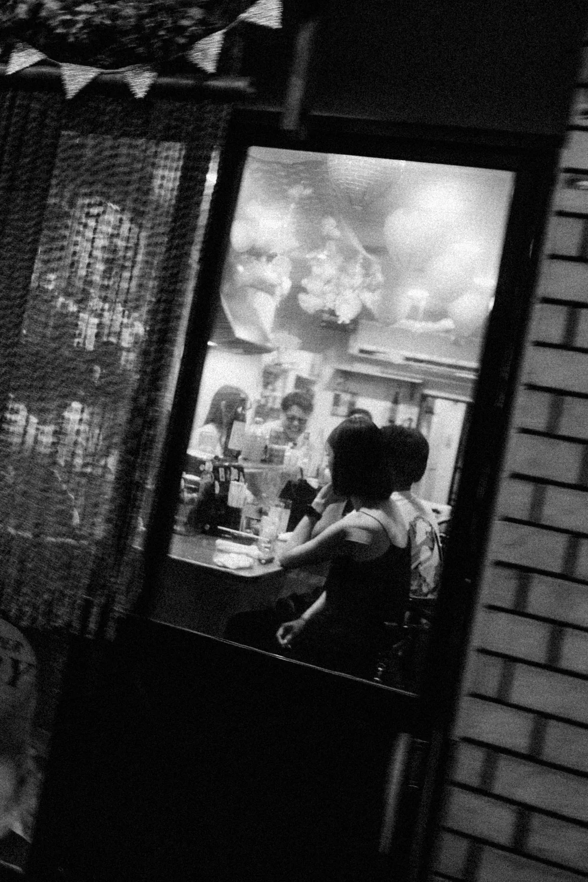 Black and white doorway view of people inside a small lit restaurant at night.