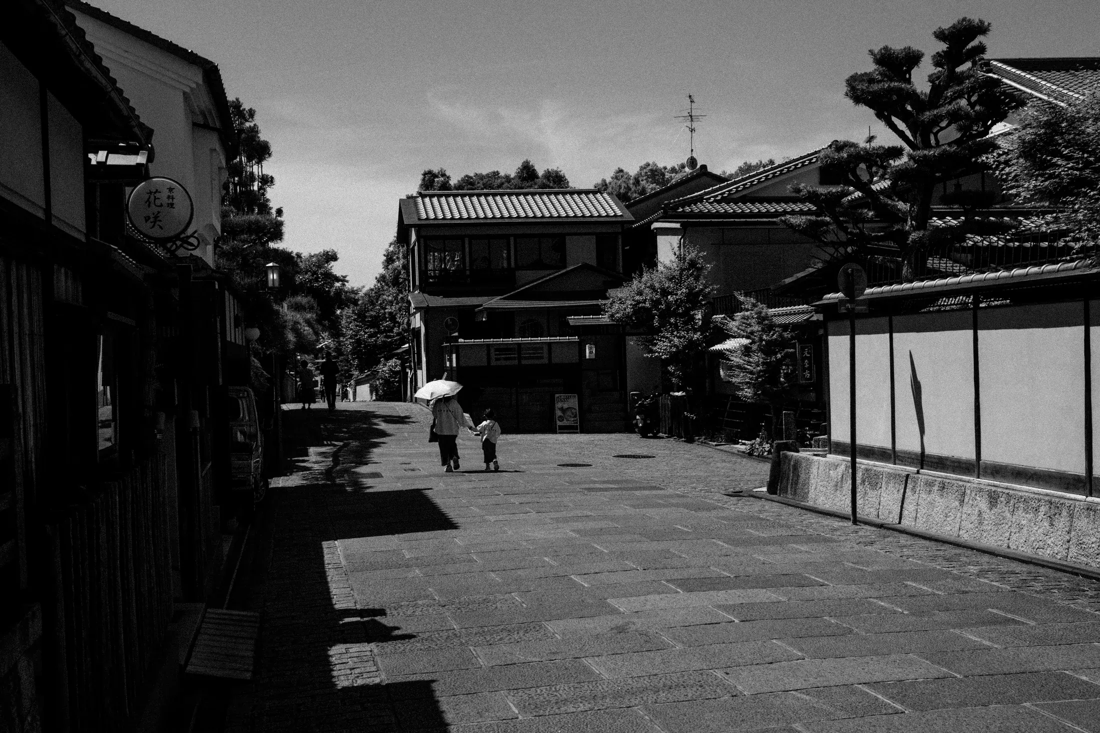 Black and white stone street lined with traditional buildings and two distant figures in bright light.
