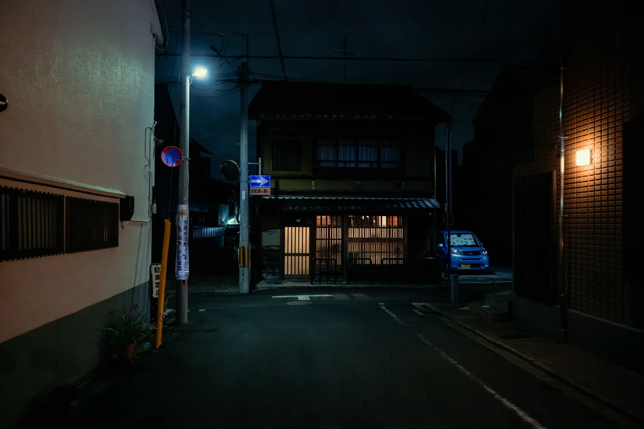 Blue night alley with a small house lit at the far end of the street.