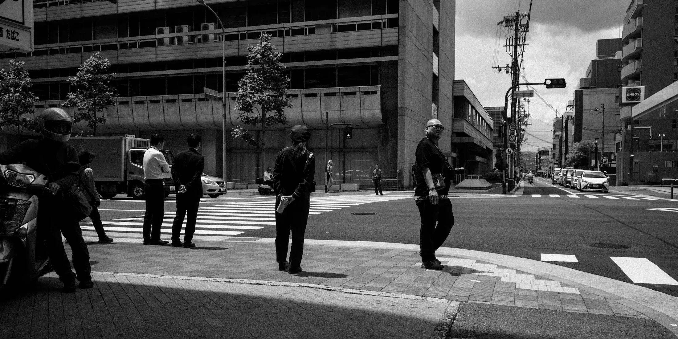 Black and white city intersection with uniformed figures waiting near a crosswalk.