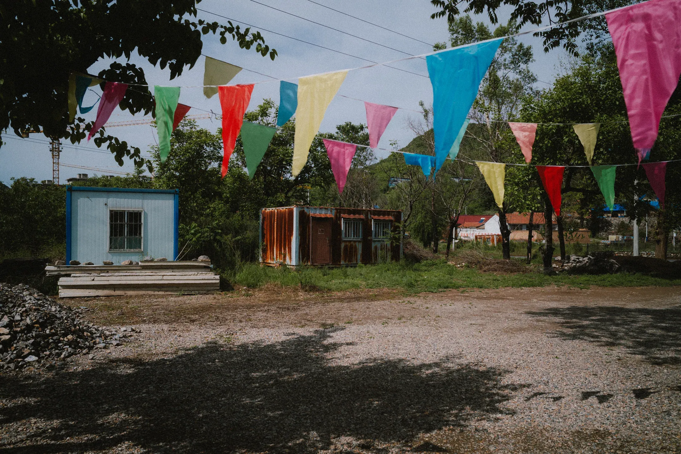 Small buildings and strings of bright flags beside a shaded yard in hard midday light.