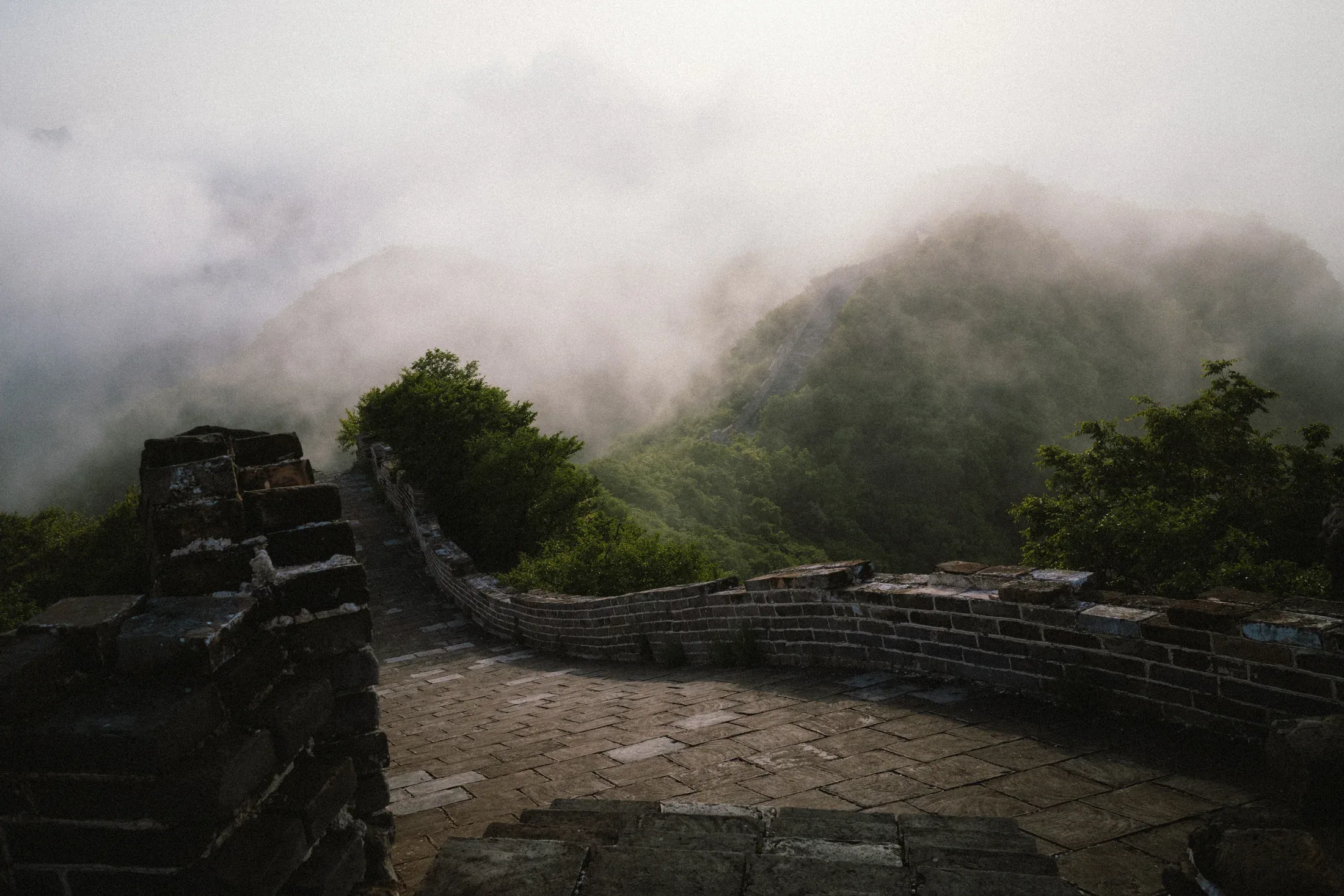 Great Wall steps descending into green mountains partly covered by low cloud.