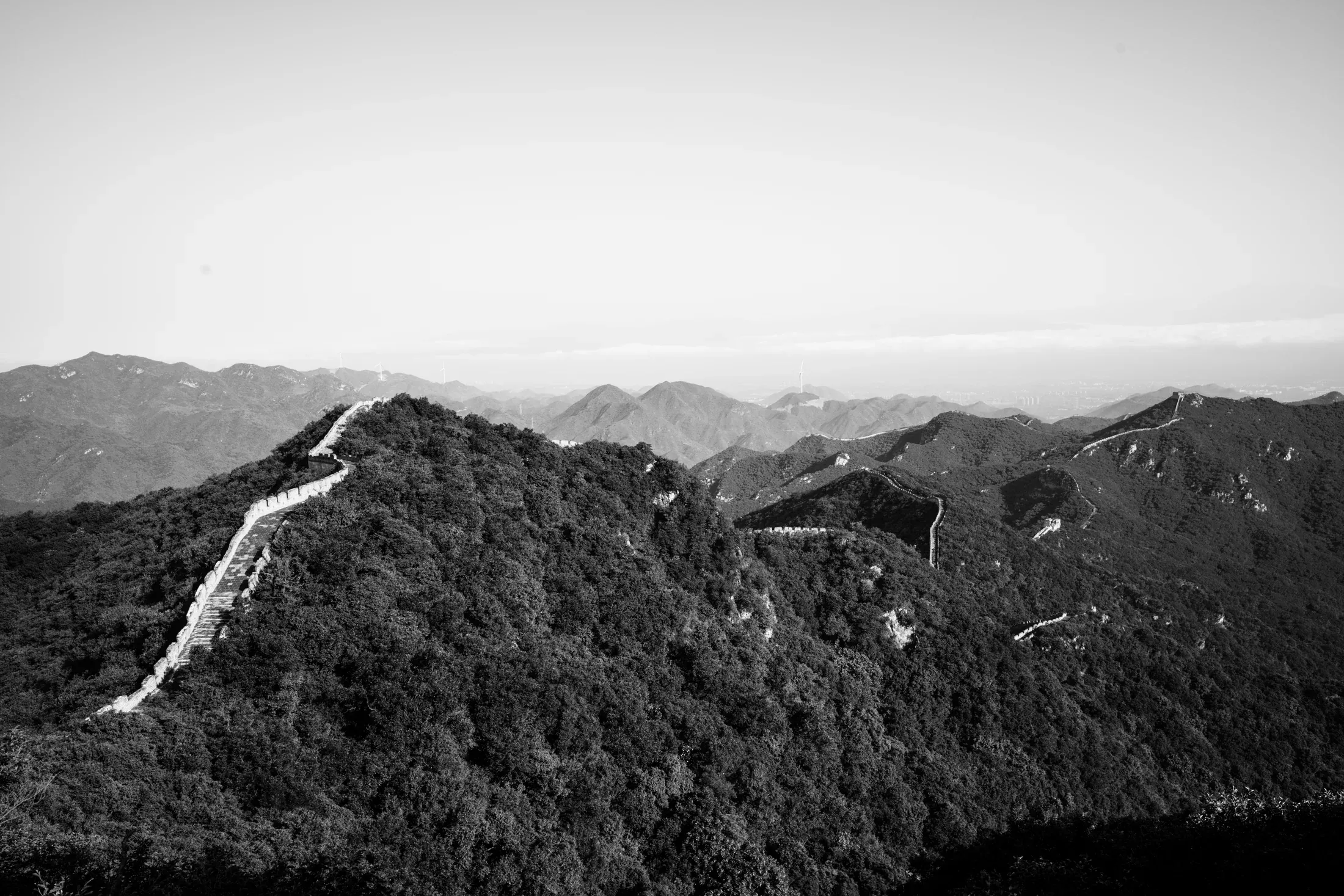 Black and white view of the Great Wall tracing a bright line over a wooded ridge.