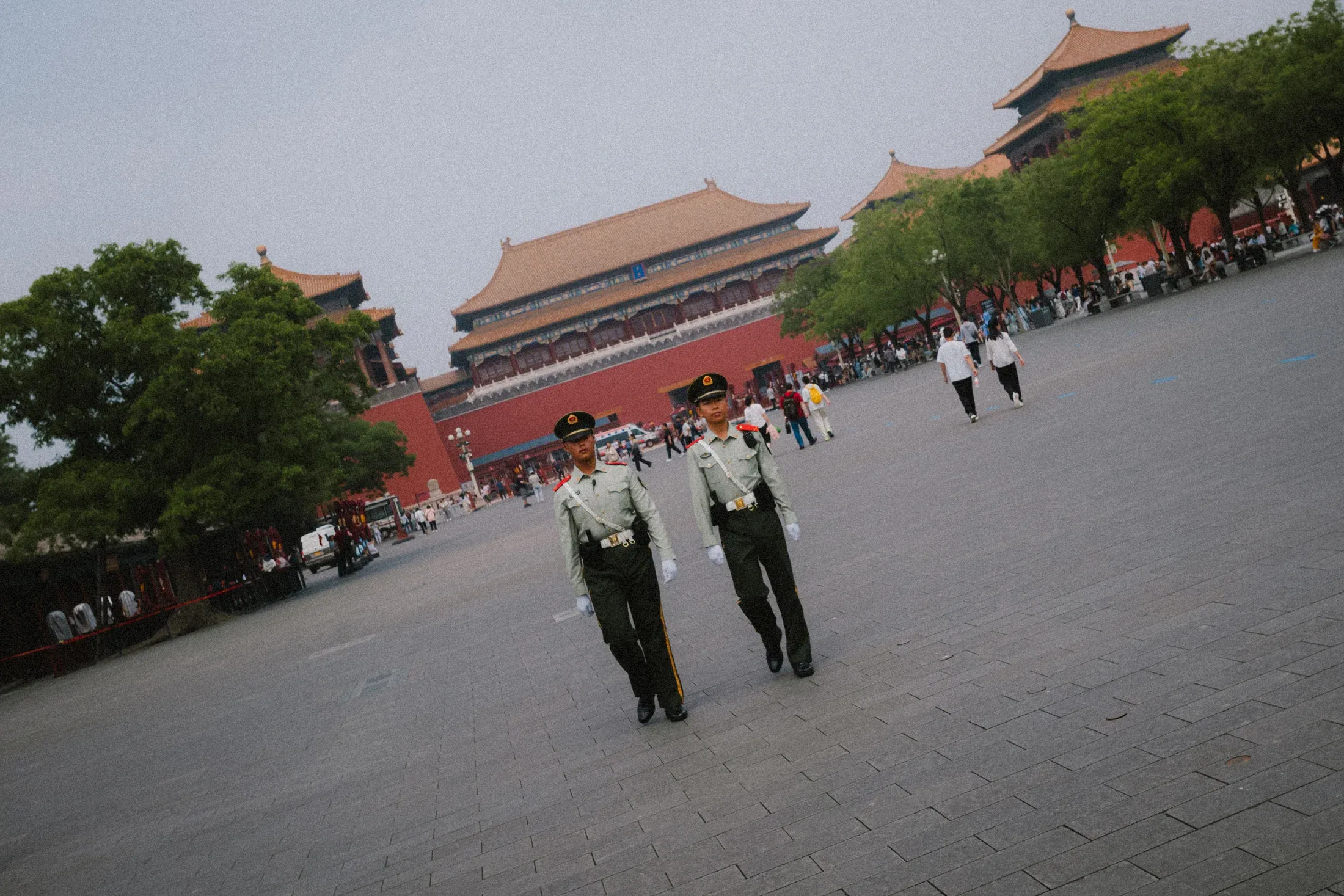 Two uniformed guards standing in a wide palace square under pale sun.