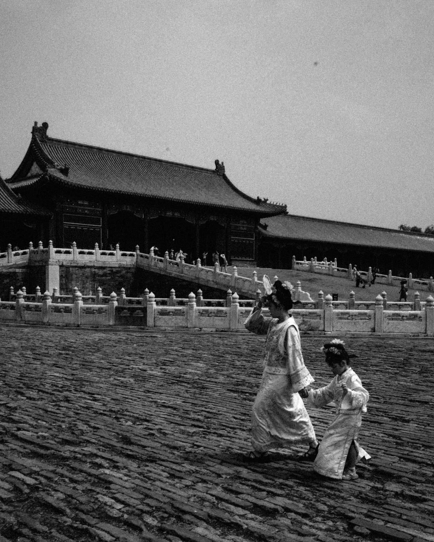 Black and white palace courtyard with two visitors crossing the stone paving.