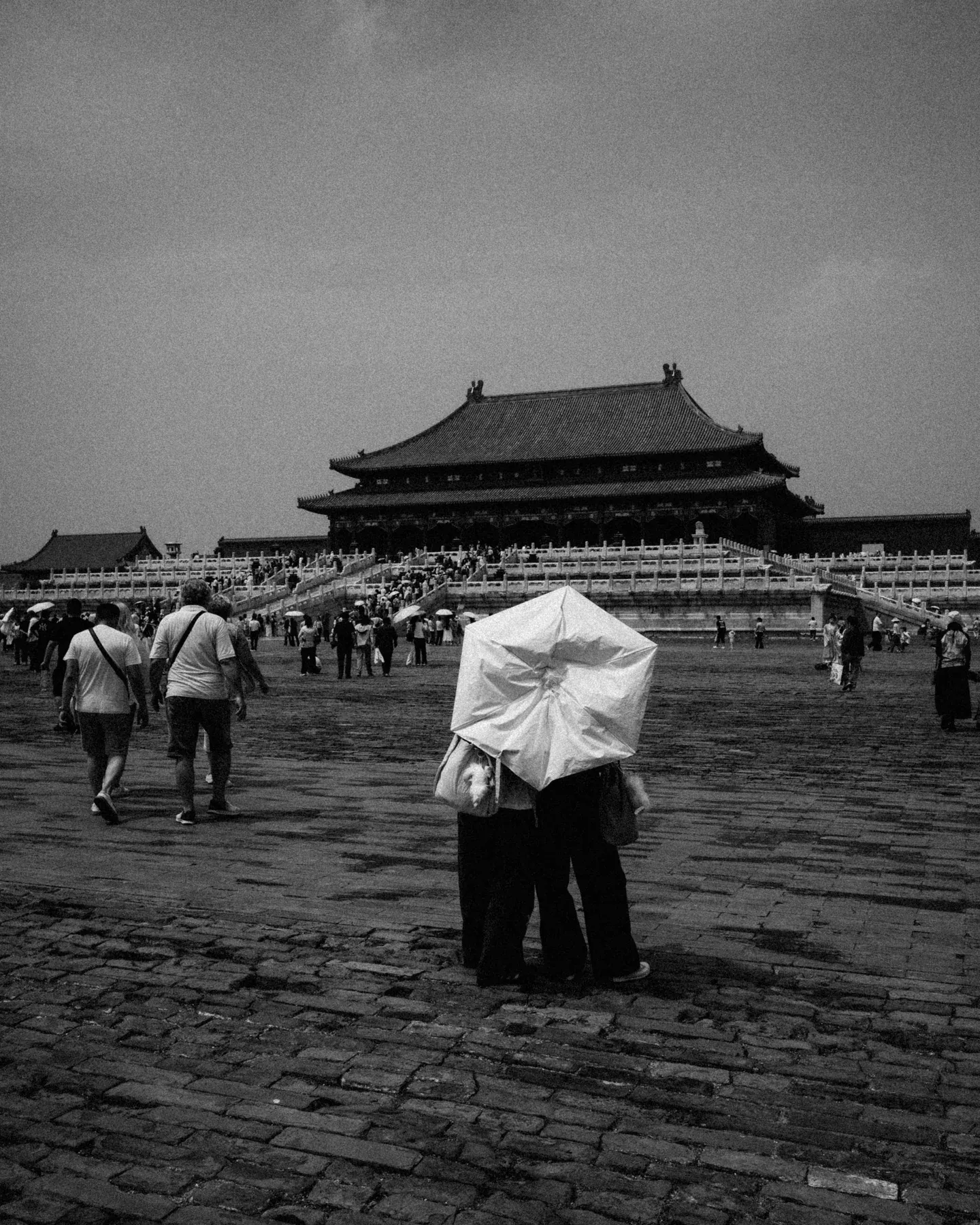 Black and white palace square with a white umbrella among groups of visitors.