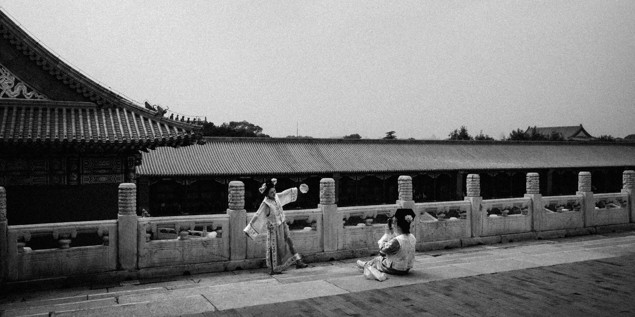Black and white palace walkway with seated visitors and figures along a stone balustrade.