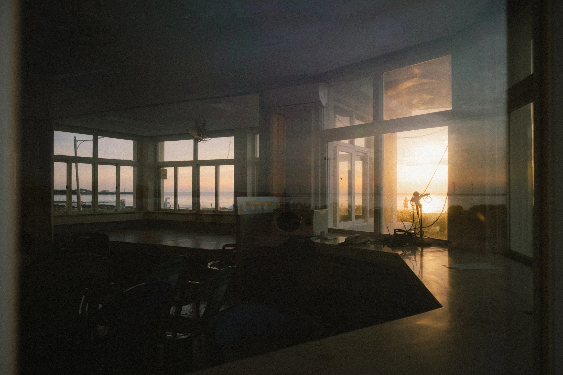 Empty seaside room reflected in glass as low sunlight enters through the windows.