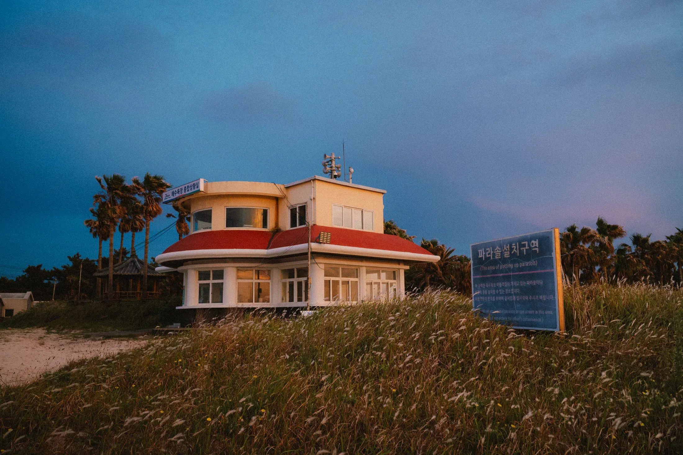 Seaside public building with a red roof beneath a deep blue evening sky.