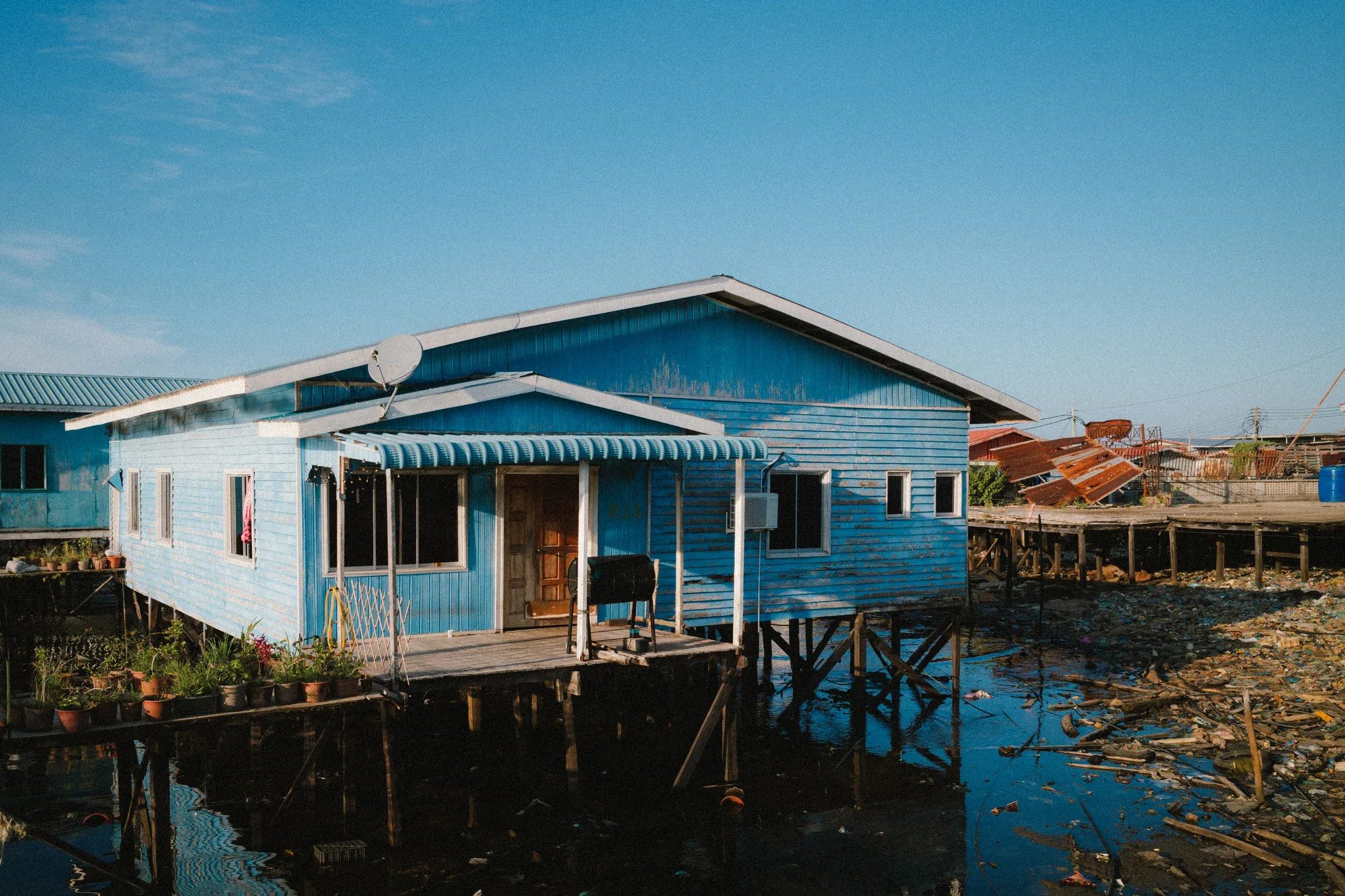 Bright blue wooden house on stilts above shallow coastal water.