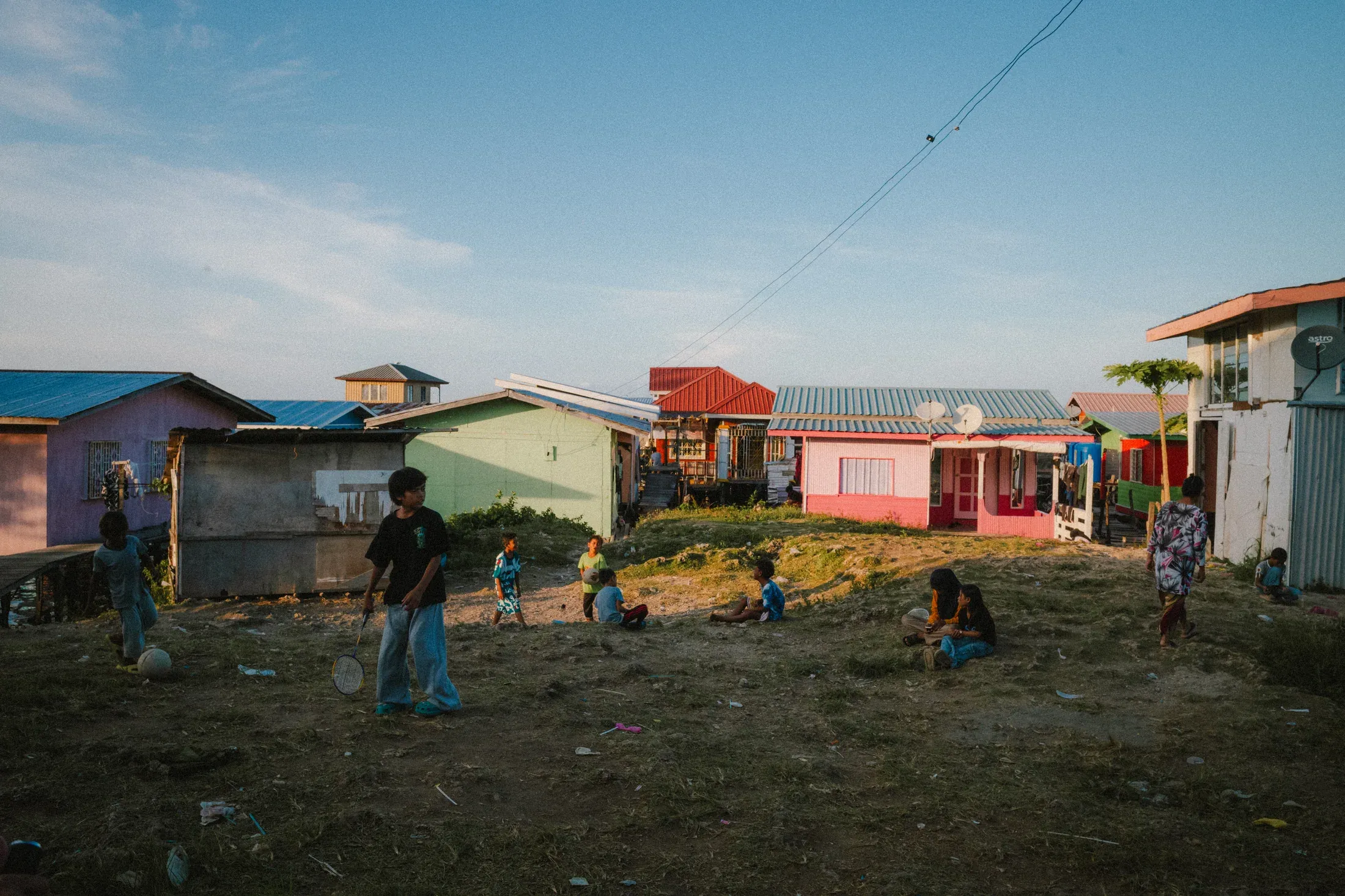 Children scattered across an open dirt yard between brightly painted houses.