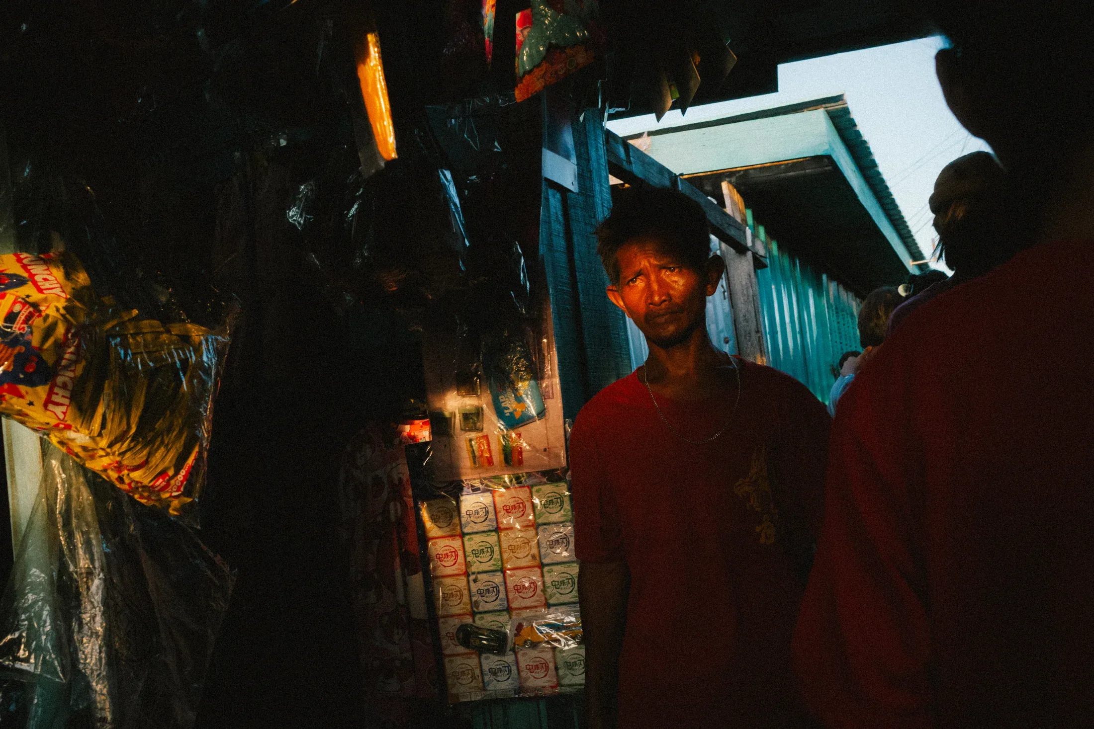 Young man standing in the warm shadow of a small shop filled with hanging goods.
