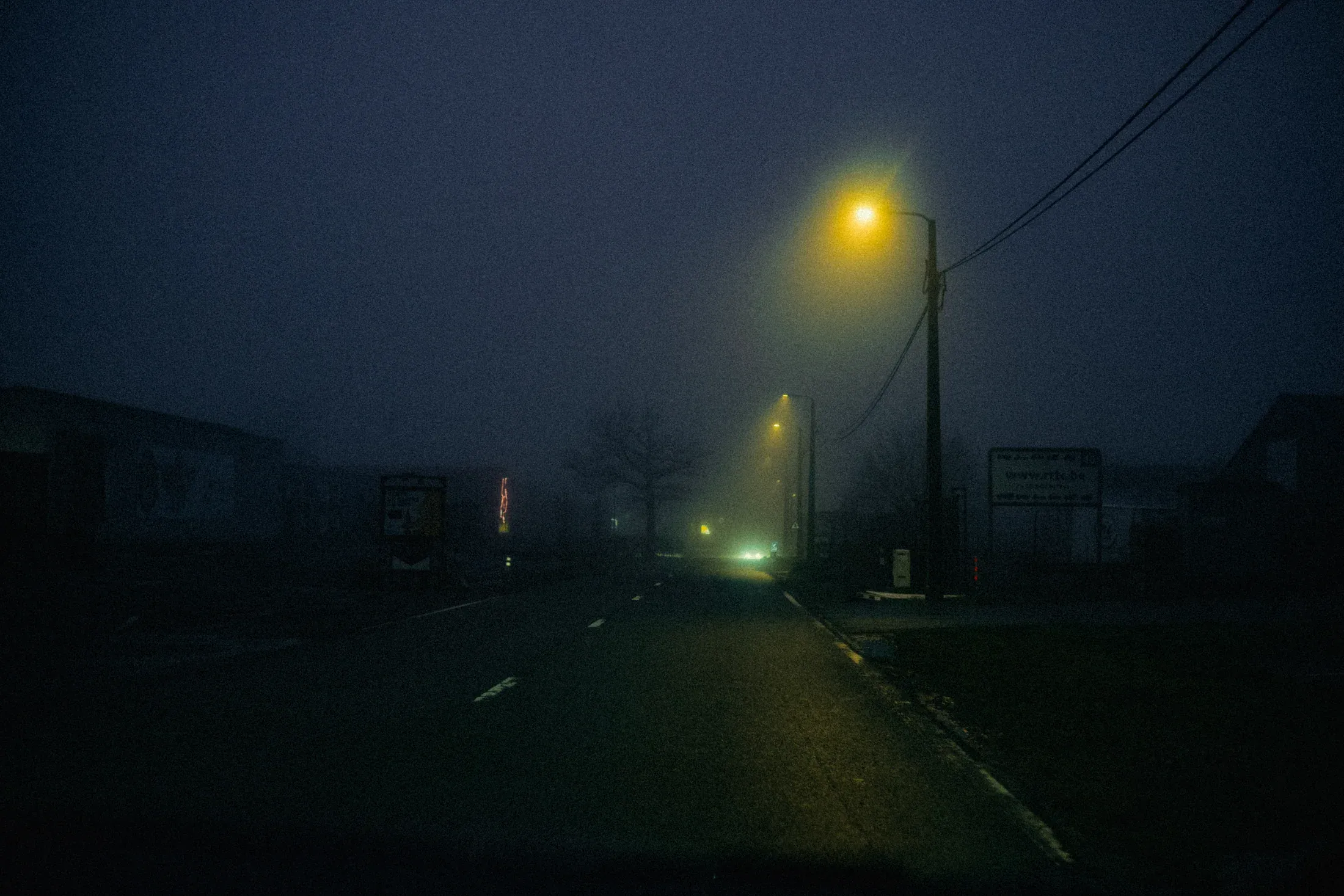 Foggy road lit by yellow streetlamps and fading green lights at night.