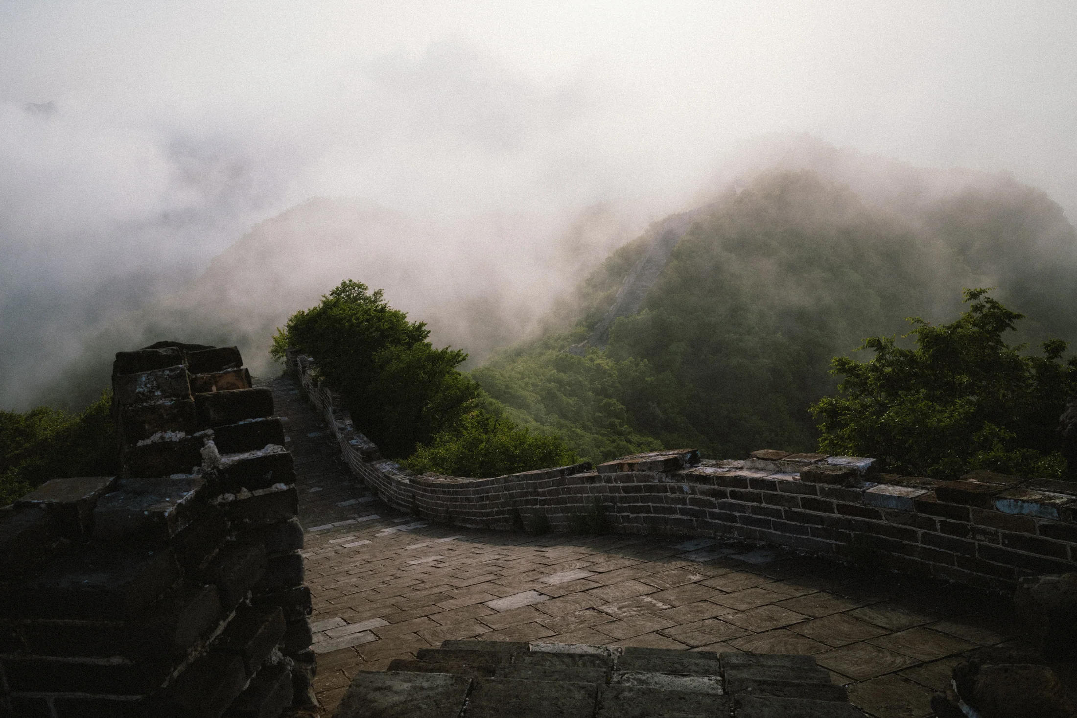 Great Wall steps descending into green mountains partly covered by low cloud.